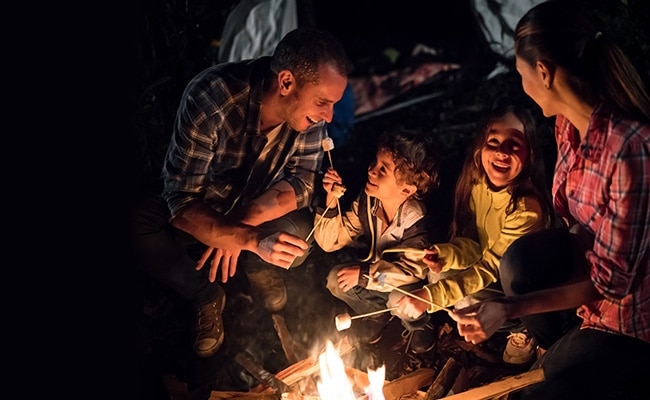 En familie med en far, en mor og to børn ved en pejs om aftenen, hvor de griller skumfiduser